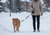 A golden retriever and their owner on a morning walk in a snowy suburban neighborhood. The owner holds a leash in one hand and looks down at the dog with a half-smile, half-sigh expression. Soft natural light, neutral tones.